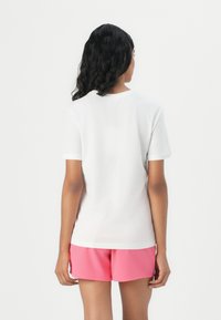 White short-sleeve t-shirt with a round neckline, paired with pink shorts. The fabric appears smooth with a fitted silhouette, viewed from the back.