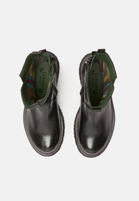 Botas de cuero negras hasta el tobillo con suelas texturizadas, paneles laterales elásticos y un forro interior de rayas coloridas. Acento metálico cerca del talón.