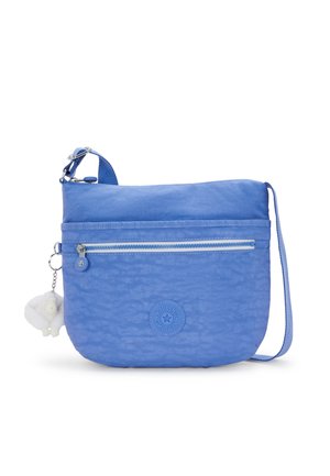 Light blue crossbody bag made of textured nylon, featuring a zippered front pocket, a round logo patch, and a small plush charm attached.