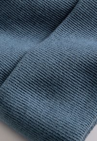 Woven fabric in a muted blue tone, featuring a textured pattern with a ribbed finish, showing fine stitches and a soft appearance.