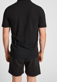 Black polo shirt made of cotton, featuring a classic collar and short sleeves, paired with black shorts. Simple, solid color design.