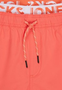Pantaloni da bagno corallo con vita elasticizzata, caratterizzati da un cordoncino decorativo con punte nere e una texture liscia. Motivi visibili all'interno.