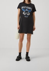Robe T-shirt grise avec le motif "WILD HEARTS", manches courtes, coupe droite, portée avec un sac à main en perles. Mocassins noirs épais et chaussettes.