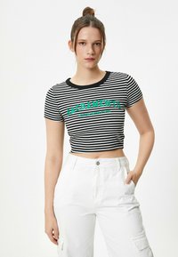 Top corto de rayas blanco y negro con mangas cortas, que presenta "SACRAMENTO" en letras verdes en negrita. Lleva pantalones blancos de talle alto.