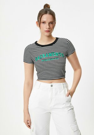 Sort og hvid stribet crop top med korte ærmer, prydet med "SACRAMENTO" i fed grøn skrift. Bæres med hvide højtaljede bukser.