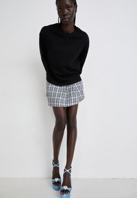Black long-sleeve shirt, grey plaid mini skirt, and blue platform sandals with heart-shaped accents. Smooth fabric and tailored fit.