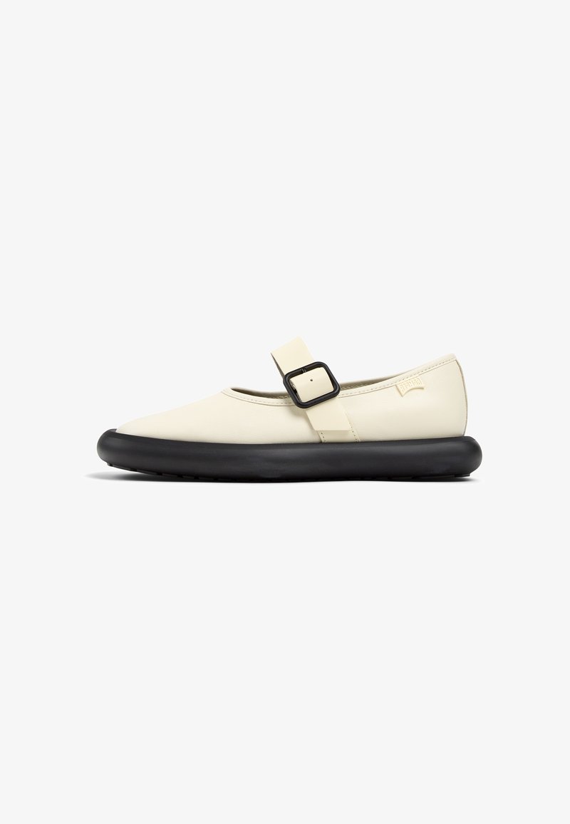 Zapato ligero de color crema con punta redondeada, suela de goma negra y una hebilla de correa negra cruzando el pie. Textura suave.