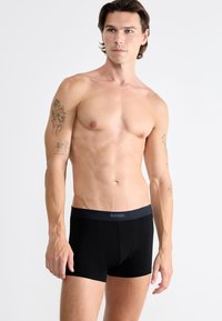 Boxer slip neri SLOGGI con una vita elastica, caratterizzati da un logo discreto sulla cintura. Il tessuto appare liscio e leggero.
