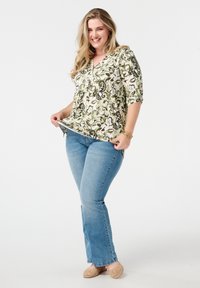 Bloemmotief, kort mouwtop in groene, crèmekleurige en zwarte tinten, gecombineerd met lichtgewassen flared jeans en beige gevlochten ballerina's.