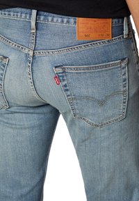 Vaaleansiniset farkut suoran mitoituksen kanssa, joissa on hillitty kuluminen, takataskut ja ruskea nahkainen logo vyötäröllä.