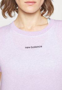 Purple cotton T-shirt featuring a crew neck and short sleeves, with a black "new balance" logo printed on the front. Soft texture.