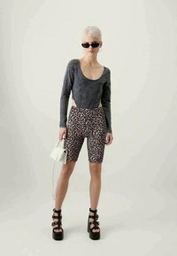 T-shirt cinza de mangas longas, calções de bicicleta com padrão de leopardo, sandálias de plataforma pretas com alças, bolsa branca e óculos de sol.