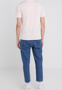 Maglietta rosa chiaro a maniche corte con scollatura rotonda, abbinata a jeans in denim blu con vestibilità comoda e gambe leggermente affusolate.