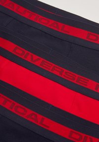 Granatowe i czerwone bawełniane szorty bokserskie z szerokimi elastycznymi pasami z napisem "DIVERSE" i "NAUTICAL" w kontrastowych kolorach.