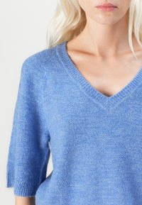 Blue knit sweater with a V-neck, short sleeves, and ribbed accents. The fabric has a soft, textured finish.