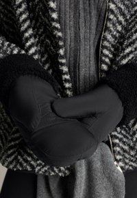 Mănuși negre impermeabile, cu un design pufos și accente cusute, purtate pe un pulover texturat gri și o jachetă cu un model alb-negru.