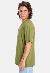 Olivově zelené bavlněné tričko s krátkým rukávem, volným střihem a potištěným grafikou na přední straně. Výrazné detaily šití a logo štítek.