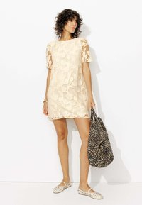 Robe en dentelle beige à manches courtes, motif floral, longueur au-dessus du genou. Accessoirisée avec un sac à imprimé léopard noir et beige.