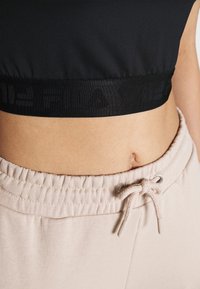 Cropped top nero con elastico e logo impresso, abbinato a pantaloni della tuta beige con coulisse e finitura testurizzata.