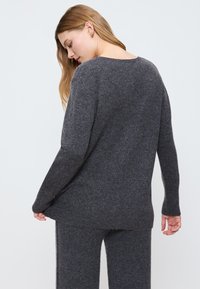 Dunkelgrauer, oversized Pullover aus weichem Material mit langen Ärmeln, rundem Halsauschnitt und geripptem Saum. Kombiniert mit passenden strukturierten Hosen.