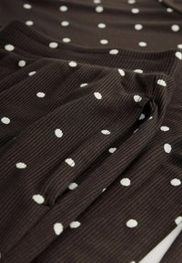 Material ribbed maro cu buline albe, având o textură moale și o formă relaxată, ideal pentru îmbrăcămintea casual.