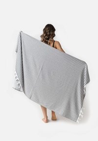 Manta a rayas en colores gris y blanco, textura suave y borlas decorativas en un borde, sostenida por una persona.
