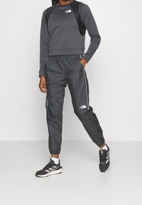 Tmavě šedá mikina se strukturovanou texturou a černými panely na ramenou, kombinovaná s černými tepláky s bočními zipy a reflexními detaily.