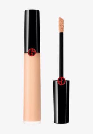 Anti-cernes liquide dans un tube noir arrondi et transparent avec une finition brillante. Présente un applicateur souple et un logo rouge bien en évidence. Teinte pêche clair.
