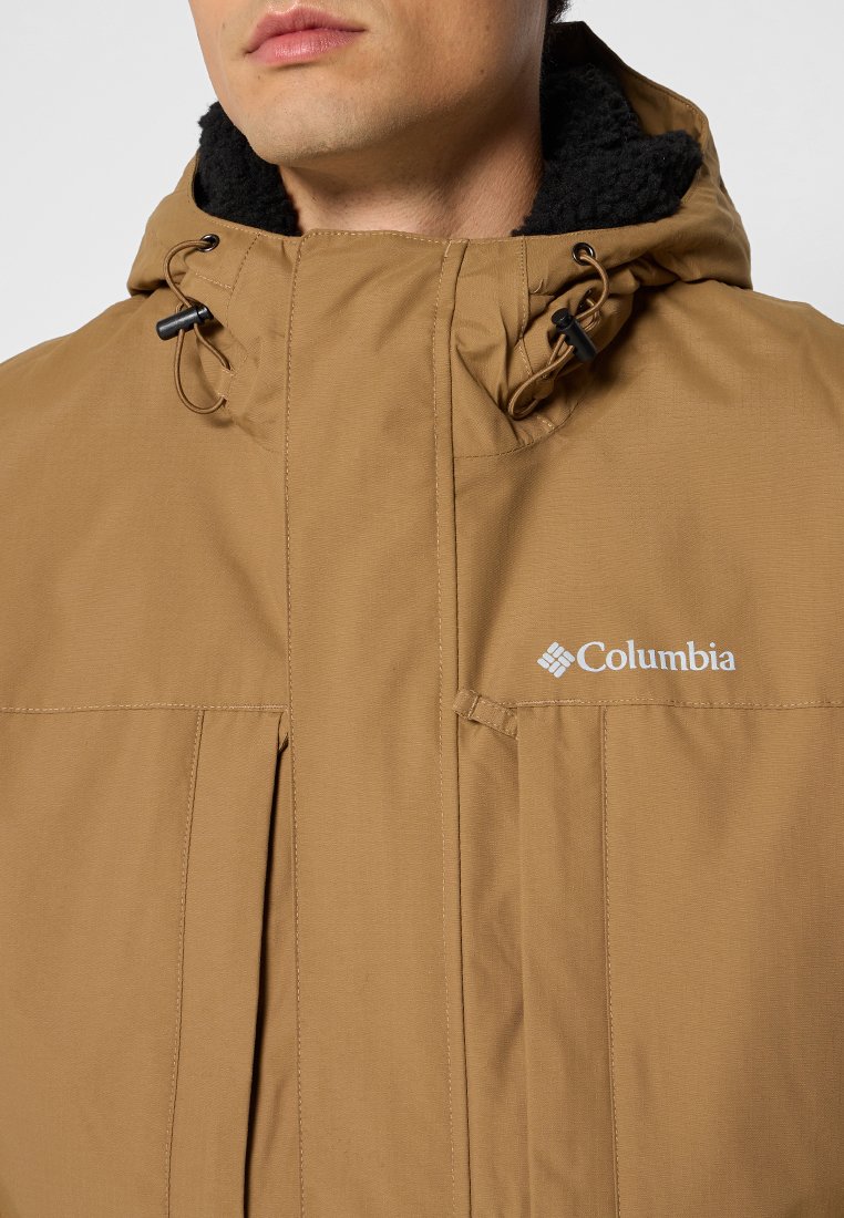 Veste Columbia marron avec une capuche texturée doublée en polaire et deux poches avant, ornée d'un logo bien visible sur la poitrine gauche.