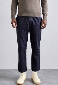 Marineblauwe broek van gladde stof met een getailleerde pasvorm, gecombineerd met crèmekleurige sneakers met een textuurdesign en lichte tinten.