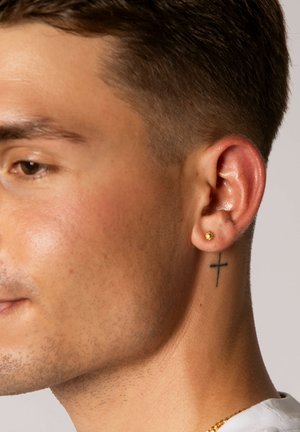 Goldene Steckerohrringe mit Sonnenstrahlen-Design, am linken Ohr getragen. Nahaufnahme der Hautstruktur, kurzer Haarschnitt und ein Kreuz-Tattoo am Hals.