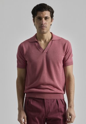 Polo de punto de manga corta en rosa claro con escote en V y puños acanalados, combinado con pantalones rojo oscuro de corte relajado.