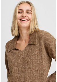 Rudas megztinis su V formos iškirpte ir apykakle, minkšta tekstūra ir visame megztinyje esantis raštuotas modelis.