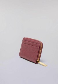 Portafoglio compatto di un tessuto testurizzato di colore rosa scuro con tasche esterne per carte e una chiusura con zip dorata, poggiato su una superficie grigia chiara.