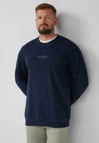 Felpa blu navy realizzata in tessuto morbido, con scollatura rotonda, polsini a coste e un logo discreto al centro. Texture liscia e vestibilità rilassata.