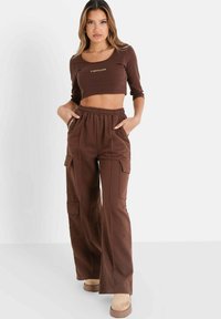 Brun cropped langærmet top med logo, parret med brune cargo bukser med elastisk talje, side lommer og en afslappet pasform.