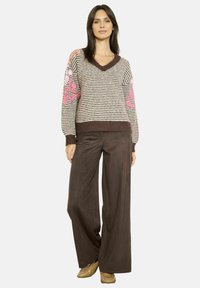 Maglione lavorato a maglia con strisce marroni e crema, dettagli floreali rosa sulle maniche, scollatura a V, abbinato a pantaloni larghi marroni.