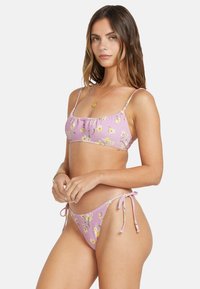 Pink floral bikini with thin straps, featuring a ruched top and adjustable tie-side bottoms. Displays a wavy, textured pattern.