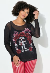 Langærmet sort mesh-top med et farverigt design af et Day of the Dead-skelet omgivet af roser, parret med røde stribede leggings.