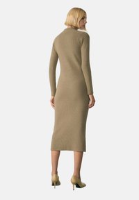 Rochie tricotată lungă, ajustată, cu tiv cu rigle, de culoare bej deschis, cu mâneci lungi și lungime până la jumătatea gambei, asortată cu pantofi cu toc înalt bej.