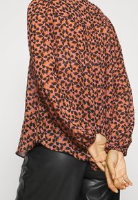 Blus med långa ärmar i rosa och svart blommönster, tillverkad av lättviktig tyg, med en samlad halsringning och elastiska mudd.