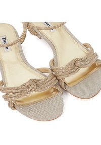 Strappy sandals with a glittery gold finish, featuring intertwined diamond-like accents and a smooth, metallic lining. Open-toed design.
