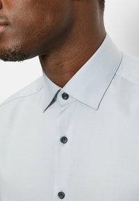 Hellgraues kurzärmliges Hemd mit einem Button-Down-Kragen, schwarzen Knöpfen und einer glatten Textur. Nahaufnahme, die den Kragen und die Knöpfe hervorhebt.