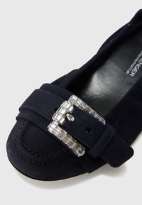 Mornarsko plava ravna cipela od brušene kože s okruglim vrhom, ukrašena srebrnom kopčom s pravokutnim detaljima i prošivenim ukrasima na gornjem dijelu.