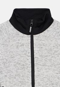 Γκρι και μαύρο μπουφάν με φερμουάρ και ψηλό γιακά, με υφή υφάσματος σε ανοιχτό γκρι και λείο μαύρο τμήμα στον λαιμό. Κλείσιμο με φερμουάρ.