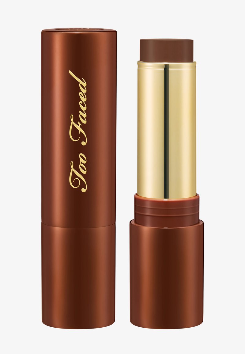 Brown creamy stick foundation with gold and brown cylindrical packaging, one closed and one open showing the product inside.