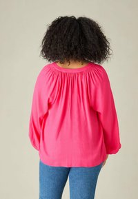 Långärmad blus i stark rosa med smockat nederkant och lös passform. Har samlade detaljer vid axlarna och mjukt, lätt tyg.