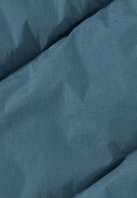 Tessuto strutturato di un blu profondo, con superficie liscia e una leggera lucentezza. Dettagli di cucitura visibili ai bordi, che mostrano un motivo trapuntato.