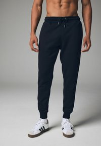 Schwarze Sweatpants mit elastischem Bund und Kordelzug. Sie verfügen über schmal zulaufende Beine und gerippte Bündchen, kombiniert mit weißen Turnschuhen.