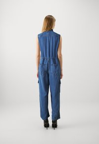 Denim jumpsuit i mellomblått med ermeles design, elastisk midje og baklommer. Har cargo-lommer på bena.